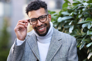 Portrait of handsome man in glasses and suit near bush outdoors