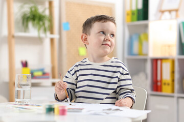 Cute little boy with brush drawing at white table indoors