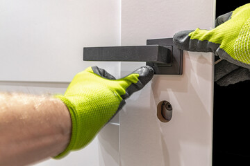Installation of a black door handle with a lock for a white wooden door,