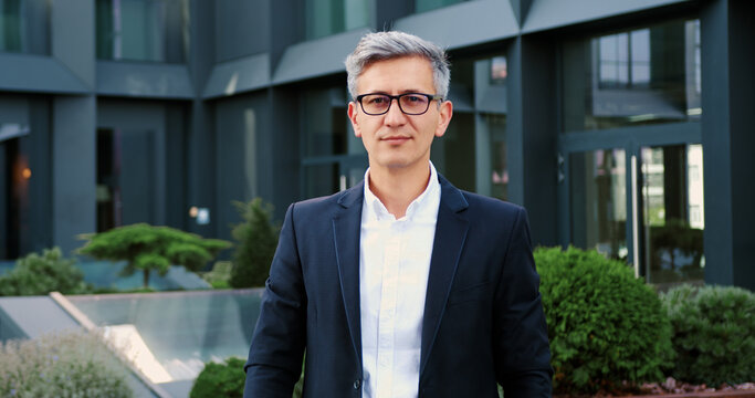 Successful confident businessman in stylish suit standing on background office building and looking inti the camera.