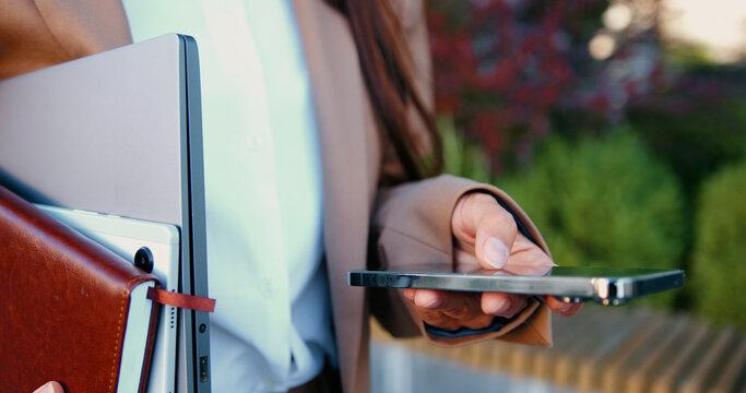 Close-up of woman hands holding a textbook and a notebook in one hand, while using her other hand to text her friends on her phone focusing on study