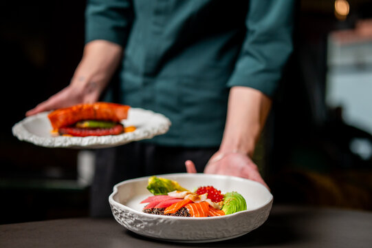 A chef presents two plates of gourmet salmon dishes with beautifully arranged fresh ingredients, showcasing fine dining and culinary expertise - Powered by Adobe