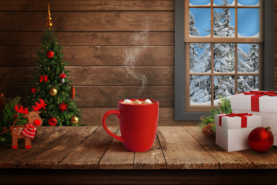 Warm Christmas scene with red mug of hot chocolate and marshmallows, decorated tree, gifts and snowy forest view through wooden cabin window