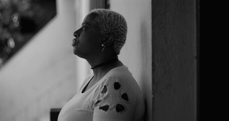 African American woman leaning against a wall, gesturing with hand, expressing despair and introspection in a monochromatic setting, themes of regret and sorrow