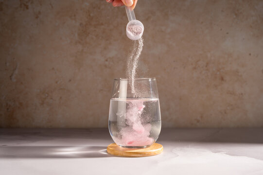 Pouring food supplement powder in glass of water. Collagen, protein powder, vitamins.