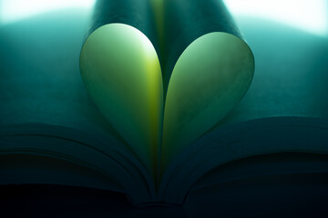 Book pages folded into a heart shape under green-blue moody lighting. Conceptual image symbolizing love for reading, imagination, storytelling and literature.