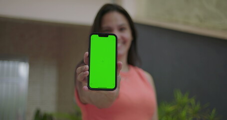 Woman extending smartphone with green screen and chroma key towards the viewer, emphasizing customizable screen, vibrant outdoor setting with blurred focus in the background