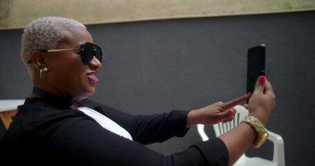 One Smiling Black woman on a video call outdoors, looking engaged and cheerful, holding a smartphone while seated in a casual setting