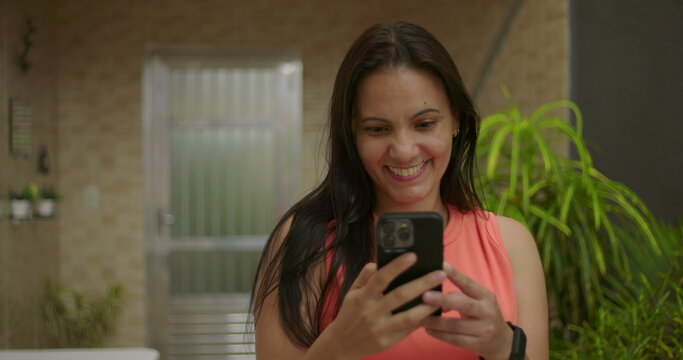 Woman smiling while looking at smartphone screen in casual outdoor setting, engaging with technology, communication, or entertainment in relaxed environment. - Powered by Adobe