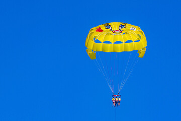 A vibrant yellow parasailing canopy with silhouetted people soars against a brilliant turquoise sky, captured in a minimalist watersports moment during high season. Antalya, Turkey.

