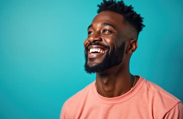Obraz premium Happy young African American man smiles widely, looks up with joy. Stylish beard, modern haircut. Positive male wears peach shirt against blue background. Confident guy expresses good mood, looking