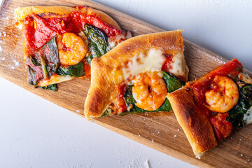 Freshly made Mediterranean pizza with shrimps on a wooden board and a white table