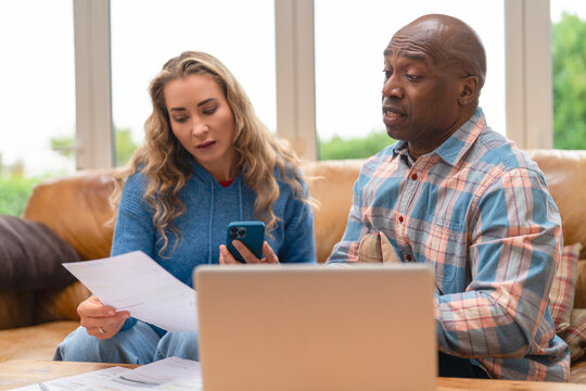 Couple discussing finances at home while reviewing documents and using a smartphone