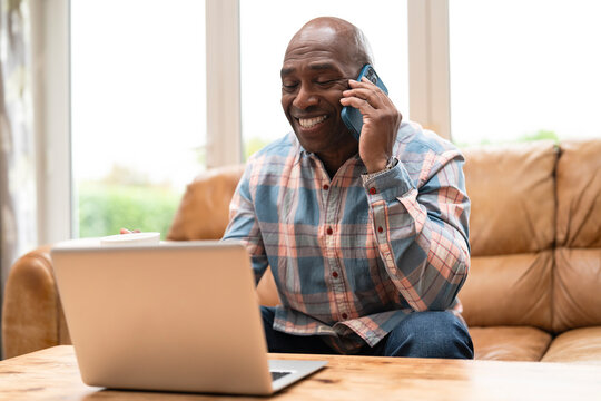 Senior man enjoying a phone call while working on his laptop in a cozy living room in the afternoon