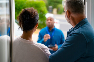Couple receives information from delivery person at their front door in a suburban neighborhood