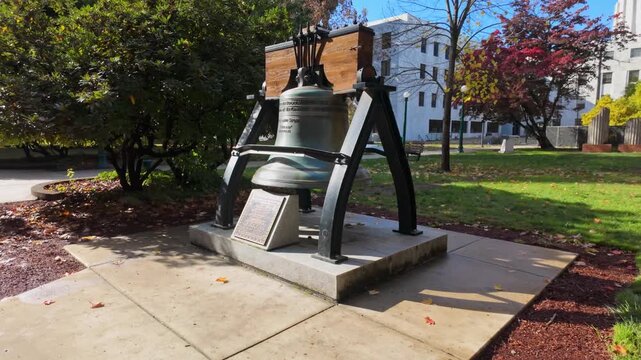 A clear view of the Liberty Bell replica displayed on the grounds of the Oregon State Capitol in Salem, with the distinctive white marble and gold-domed capitol building visible in the background.