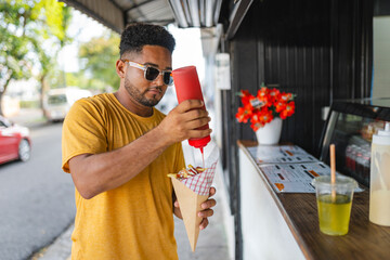 Man adding ketchup to street food fries at outdoor stand