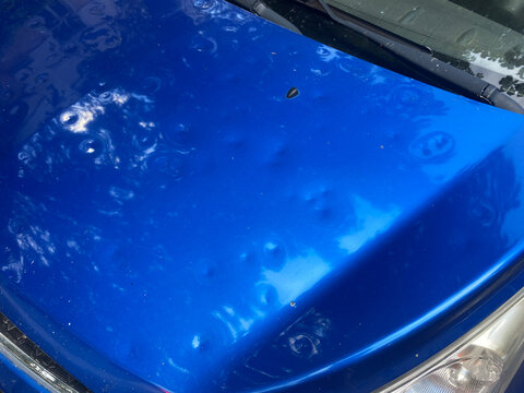 Pitted car hood after hailstorm. Close-up of dented automobile hood with hail damage. Multiple dimples and dents from hailstorm impact. Insurance, damage compensation.