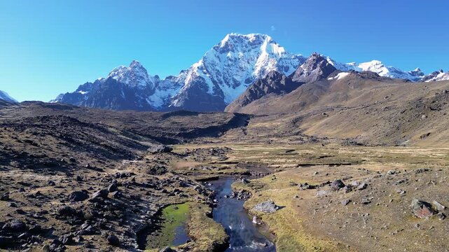 Ausangate, Peru: Forward aerial drone footage on a river on the foot hill of Ausangate, a snow-capped mountain peak in Andes Cordillera in Peru. This is a famous trekking area not far from Cusco