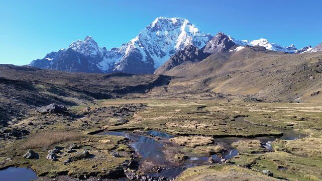 Ausangate, Peru: Orbit aerial drone footage on a river heading to Ausangate, a mountain in Andes, Peru, showing the 6,384 metres peak under a clear blue sky in early morning. 