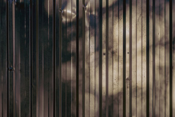 Dark corrugated metal wall metal wall with vertical lines reflecting sunlight and shadows. Industrial background with metallic texture for graphic use