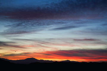 Vivid sunset sky over dark mountain silhouette with colorful clouds and gradient light in evening