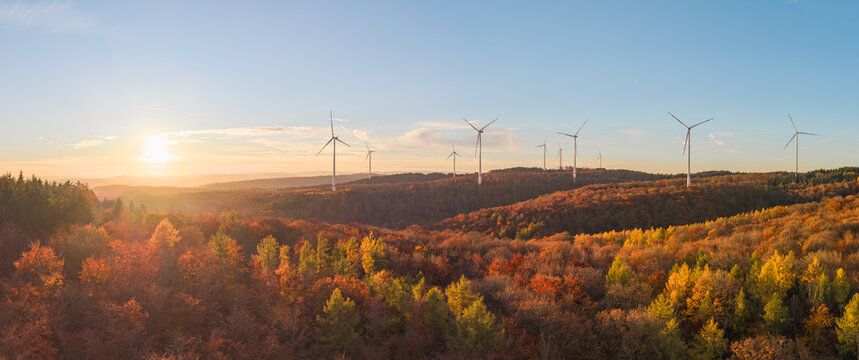 Wind turbines on the mountain between the vibrant fall forest at dusk