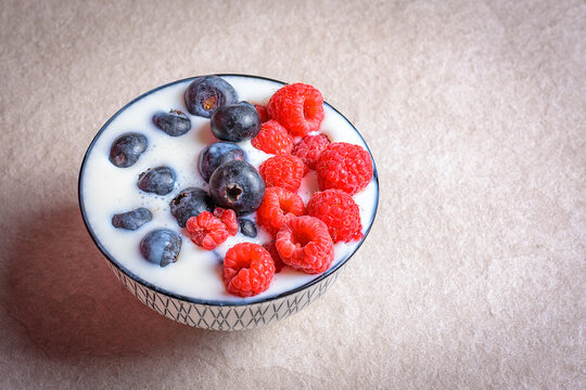 Full bowl of fresh raspberries and blueberries in milkon a light kitchen counter. Ideal for healthy breakfast, diet, superfood, and vegan lifestyle concepts with copy space