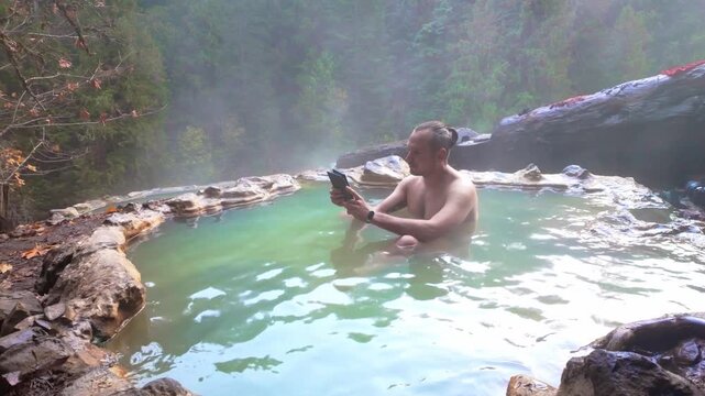 A male individual peacefully relaxing and reading a book while soaking in the natural geothermal pools of Umpqua Hot Springs, surrounded by the tranquil Oregon forest.