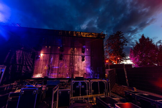 Large outdoor stage with illuminated backdrop curtains and rigging against dramatic twilight sky