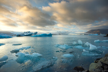 Icebergs float in Iceland's glacier lagoon, reflecting the warm colors of sunset. Birds fly above, adding life to the tranquil scene. This location is a must-see for nature enthusiasts.