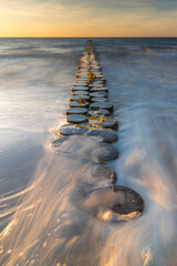 Fototapeta premium Buhnen in Wustrow an der Ostsee bei Sonnenuntergang mit Wellen in der Langzeitbelichtung