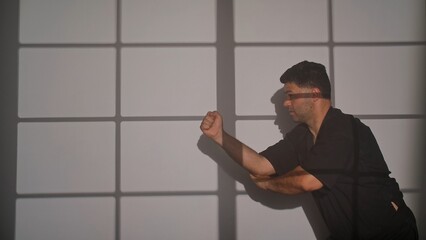 A man in a black kimono practices martial arts using shadowboxing against a light colored grid background. A man conducts training in the Chinese martial art of Wing Chun.