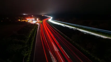 Fotobehang Snelweg In De Nacht Highway traffic light trails at night with gas station  © Dimitar