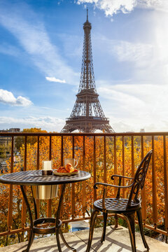 A balcony with a breakfast table and empty chair with view of the Eiffel Tower in Paris, France, during morning time and sunshine