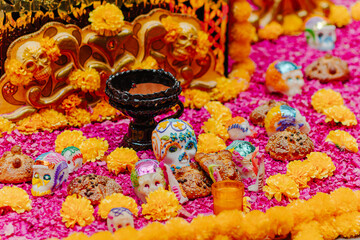 Close view of Day of the Dead offerings featuring decorated sugar skulls, Pan de Muerto (bread of the dead), and marigold flowers on a vibrant background.