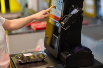 A woman weighs cucumbers at a self-service checkout. 