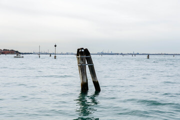 Murano, Italy - November 21, 2024: Scenic view of wooden posts emerging from calm waters near Murano Island, showcasing the serene beauty of the Venetian lagoon landscape
