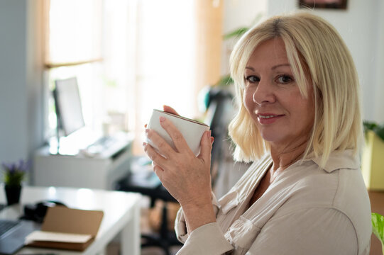 Mature woman enjoying coffee at home office taking break