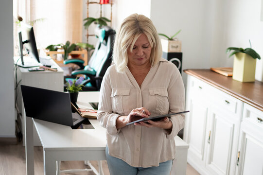 Mature woman connecting online, using tablet in home office