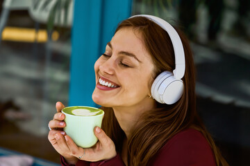 Happy Woman Wearing White Headphones Sips Green Latte Cup Outdoors Enjoying Music Cafe Moment Bright Smile