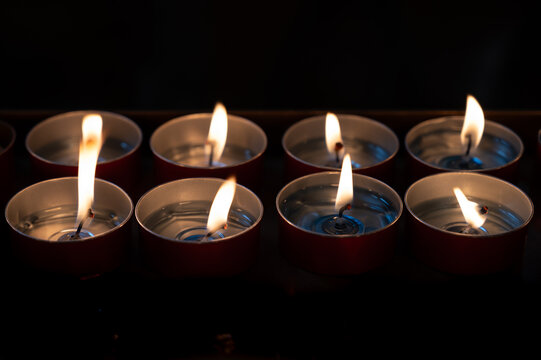 A serene close-up of burning tealight candles glowing softly in the dark, their warm flames symbolizing peace, reflection, and remembrance