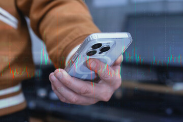 Hand holding a modern smartphone over an abstract digital background featuring financial data, stock market quotes and a glowing candlestick chart overlay.