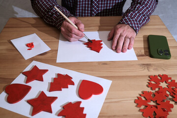 Man painting red wooden christmas decorations for holiday crafts