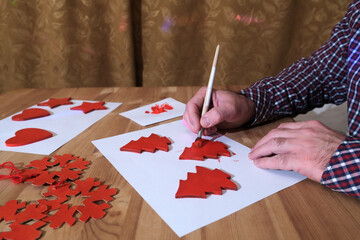 Man painting red handmade christmas tree ornaments for holiday decoration