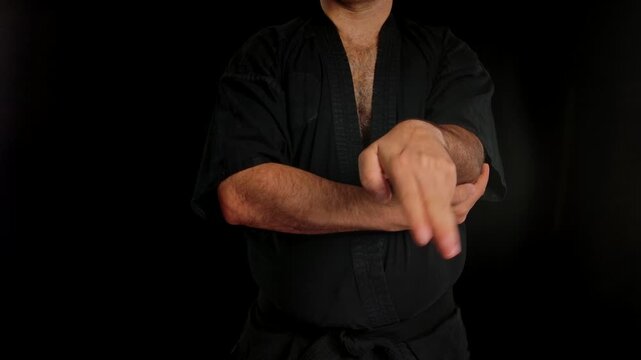 Close up of a man practicing Wing Chun in a black kimono, demonstrating Wing Chun hand and elbow control against a dark studio background, showing self defense training and martial arts techniques.