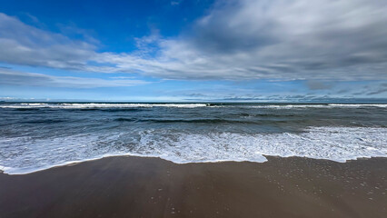Image of a beach with a horizon separating the sea from the sky. Waves break on the shore, creating...