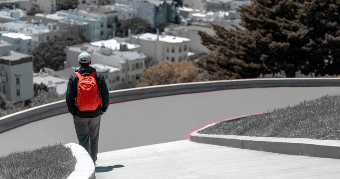 Person walking alone on a curved urban pathway with a bright red backpack and casual clothing in a cityscape setting