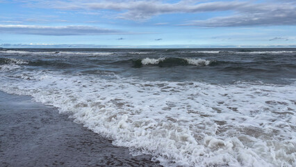 Image of a beach with a horizon separating the sea from the sky. Waves break on the shore, creating...