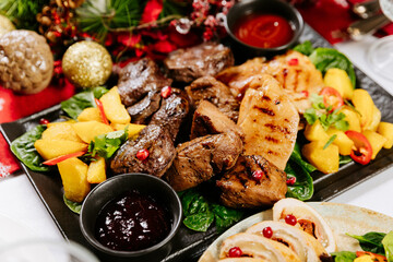 Assorted grilled meat and potatoes with sauce on festive holiday table setting
